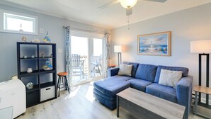 A living room with a blue sofa, a coffee table, a black shelving unit, and a ceiling fan. - Beachfront Family Condo w/ Stunning Views! (Sneads Ferry)