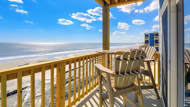 A wooden deck with a table and chairs overlooking a beach. - Beachfront Family Condo w/ Stunning Views! (Sneads Ferry)