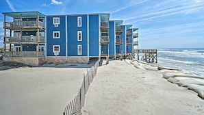 A multi-story blue building with balconies, a sandy beach in front, and a wooden pier extending into the water. - Beachfront Family Condo w/ Stunning Views! (Sneads Ferry)