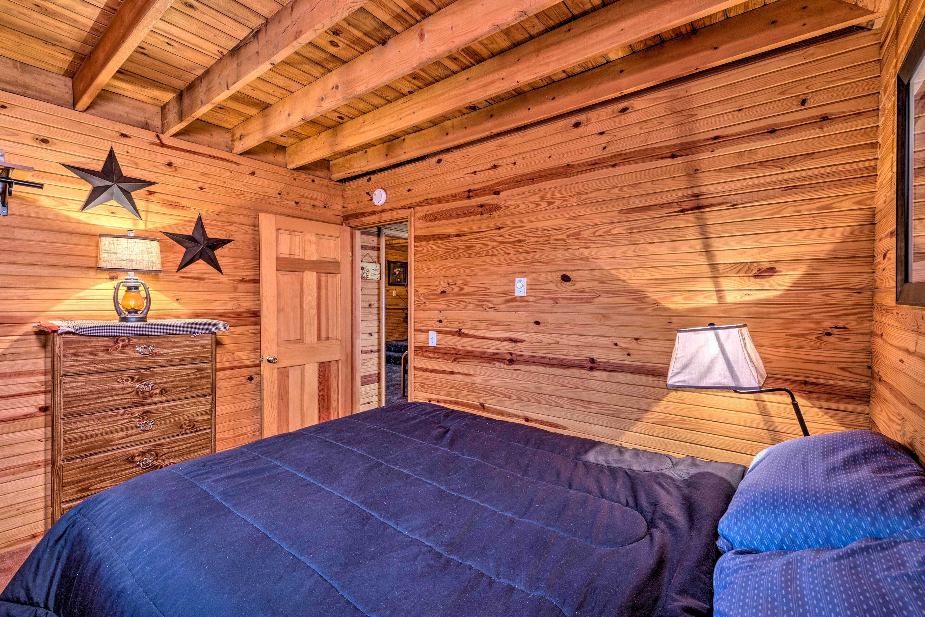 A wooden cabin bedroom with a bed, dresser, star decorations, and a lamp.