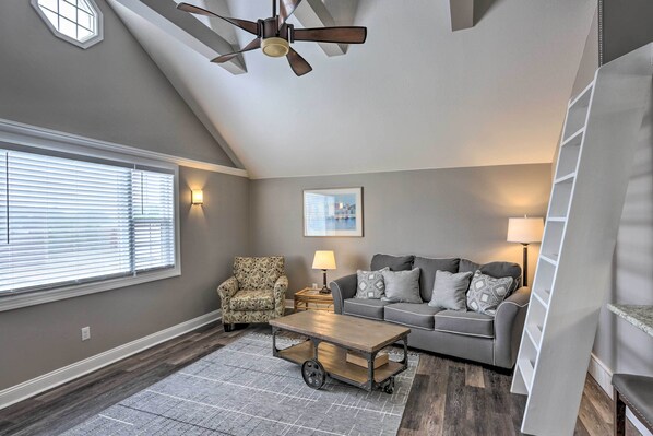A living room with a gray couch, patterned armchair, and a coffee table with wheels. - Updated Lake Erie Home ~ 34 Mi to Cedar Point! (Lorain)