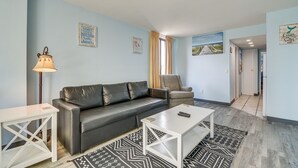 A modern living room with a black leather sofa, a white coffee table, and a patterned rug. There is a lamp, a framed picture, and a painting on the wall. - Myrtle Beach Condo w/ Lazy River: Walk to Beach! (Myrtle Beach)