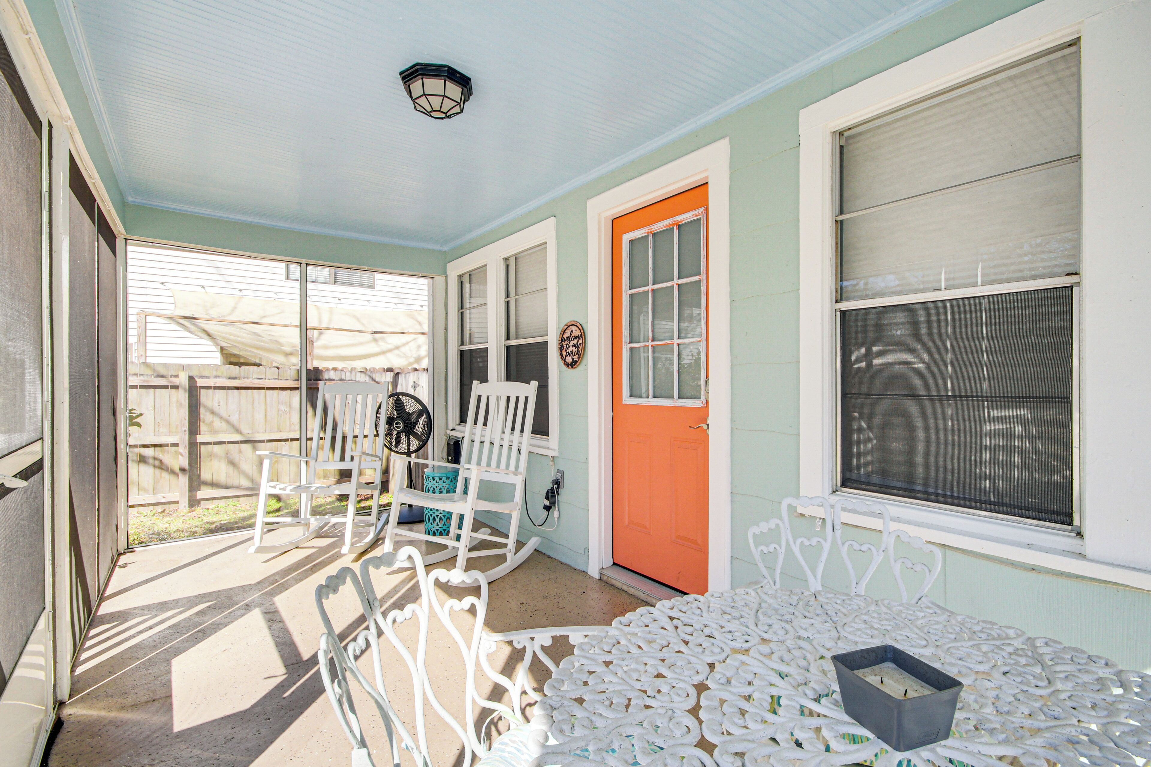 A covered porch with white metal chairs, a table, and a bright orange door.