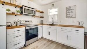 Eine moderne Küche mit weißen Schränken, einer Mikrowelle, einem Backofen und Holzarbeitsplatten. Ein Fenster bietet Blick ins Freie, und an der Wand befindet sich ein motivierendes Zitat.
