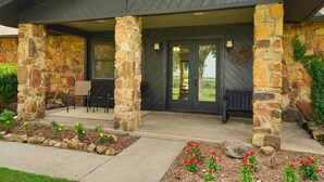 A stone-clad building with a covered patio, outdoor seating, and a flower bed. - Spacious Country Home Near Ft Sill & Medicine Park (Lawton)