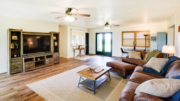 A living room with a large flat-screen TV, leather sofas, a coffee table, and a ceiling fan. - Spacious Country Home Near Ft Sill & Medicine Park (Lawton)