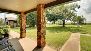 A covered patio area with stone pillars, a concrete walkway, and a view of a grassy lawn and trees. - Spacious Country Home Near Ft Sill & Medicine Park (Lawton)