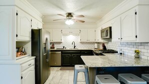 A kitchen with white cabinets, a black refrigerator, a microwave, a sink, and a ceiling fan. - Spacious Country Home Near Ft Sill & Medicine Park (Lawton)