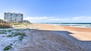 A beachfront hotel with multiple floors, a sandy beach in the foreground, and the ocean in the background. - Luxe Oceanfront Condo w/ Pool, Beach Access + Gear (Ormond Beach)