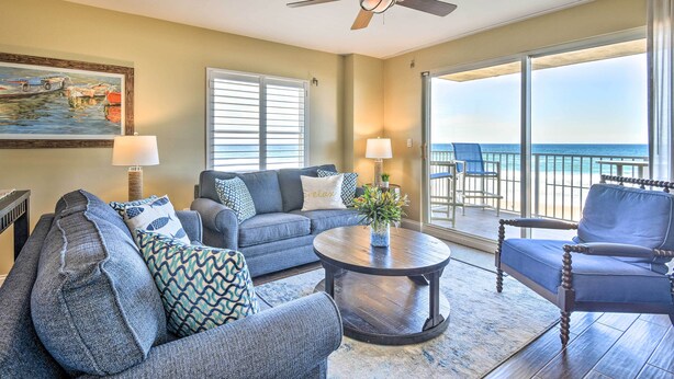 A living room with a sofa, armchair, and coffee table, a ceiling fan, and a view of the ocean through large windows. - Luxe Oceanfront Condo w/ Pool, Beach Access + Gear (Ormond Beach)