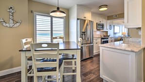 A modern kitchen with white cabinets, a stainless steel refrigerator, and a dining area with a table and chairs. - Luxe Oceanfront Condo w/ Pool, Beach Access + Gear (Ormond Beach)