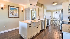 A modern kitchen with white cabinetry, a large island, and a dining area with a table and chairs. - Luxe Oceanfront Condo w/ Pool, Beach Access + Gear (Ormond Beach)