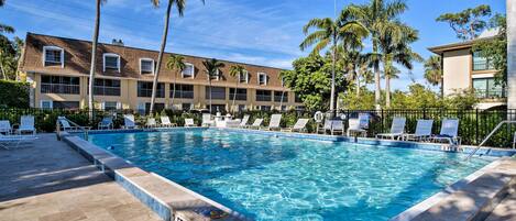 A swimming pool with lounge chairs and palm trees, surrounded by a building with multiple balconies.