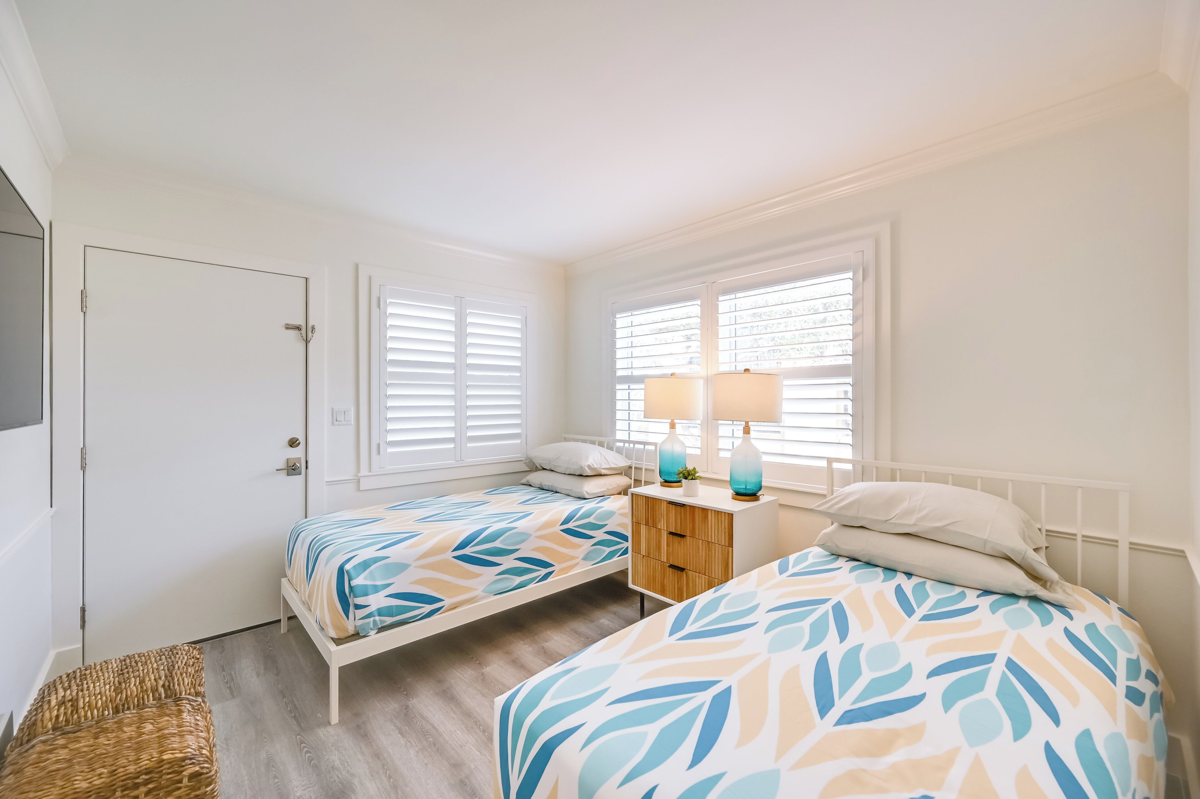 A bedroom with two single beds, a nightstand with a lamp, and a door.