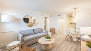 Ein modernes Wohnzimmer mit grauem Sofa, einem runden Couchtisch und einem Essbereich mit weißem Tisch und Stühlen.