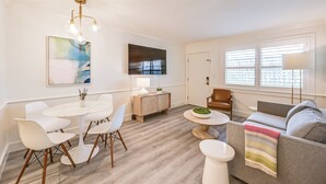 Ein modernes Wohnzimmer mit Essbereich, einem grauen Sofa, einem weißen Tisch und einem Deckenventilator.