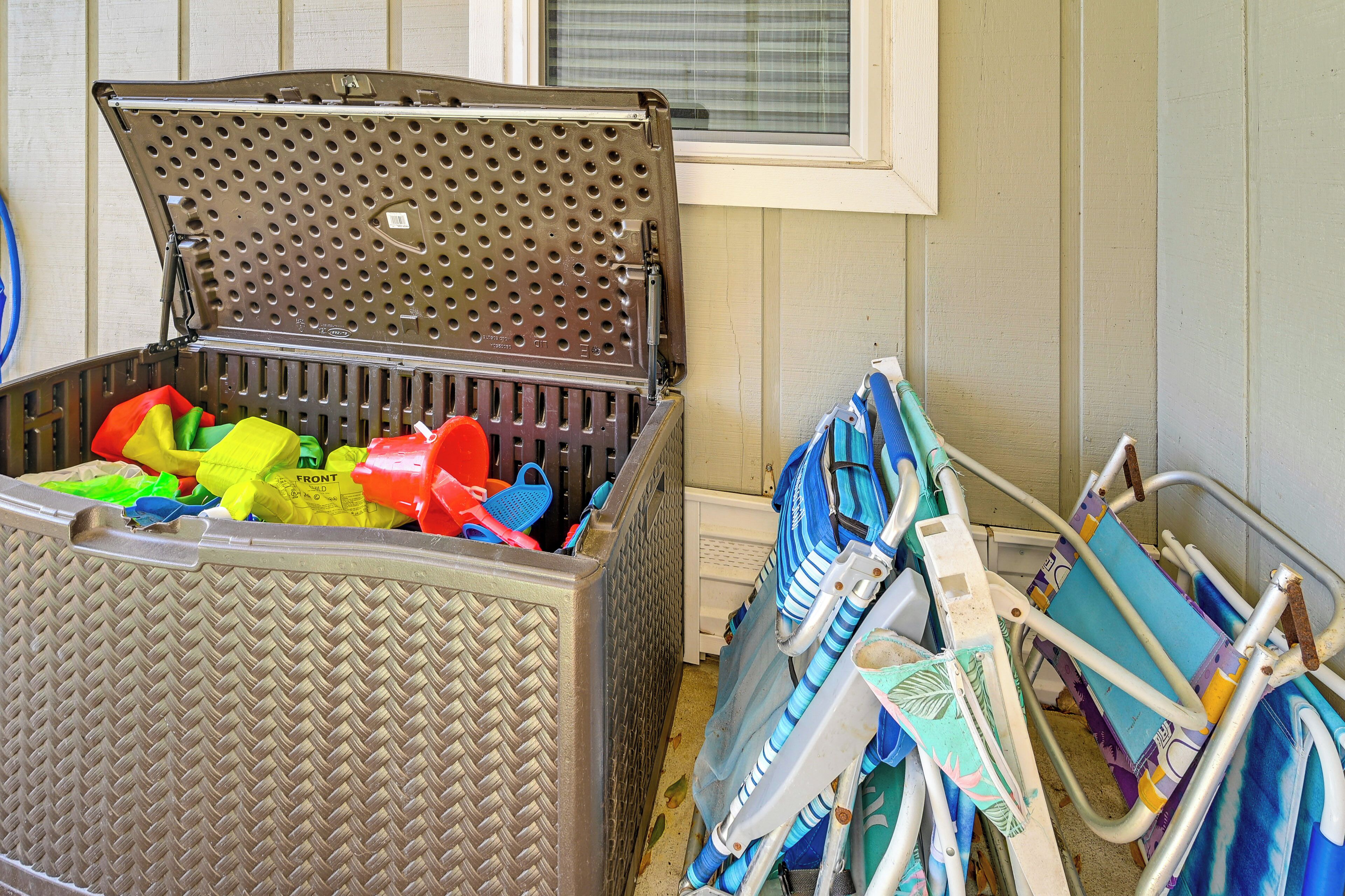 A storage bin filled with various items, including colorful bags and a stroller, next to a window with blinds.