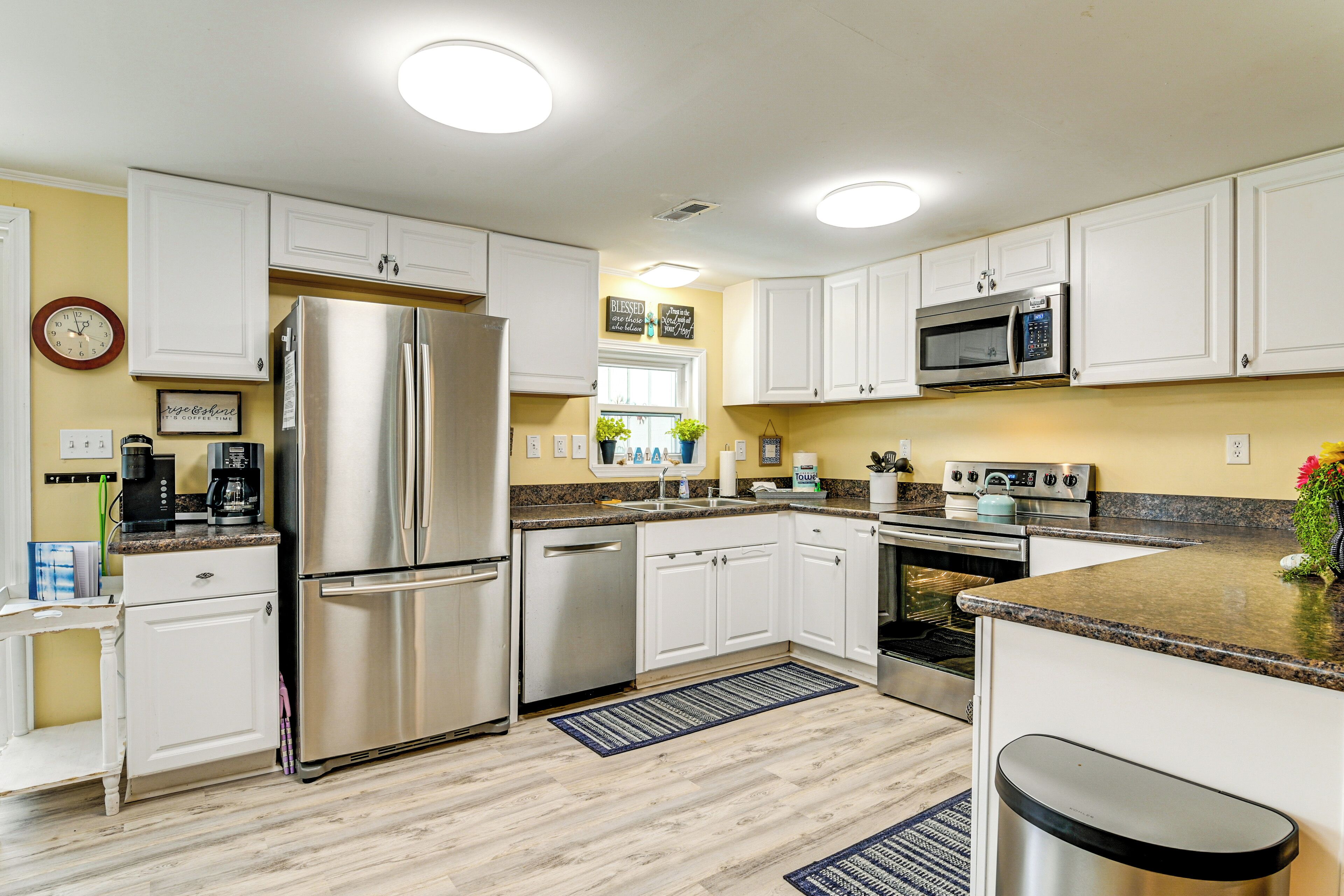 A modern kitchen with white cabinets, stainless steel appliances, granite countertops, and a clock on the wall.