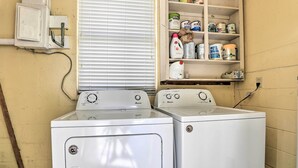 A laundry room with two front-loading washing machines, a shelf with various cleaning supplies, and a window with blinds. - Lakeland Home w/ Large Backyard ~ 1 Mile From Fsc! (Lakeland)