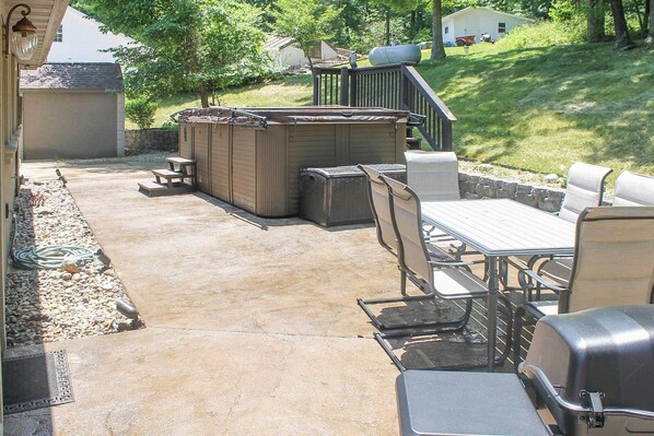 An outdoor patio with a hot tub, seating area, and a grill.