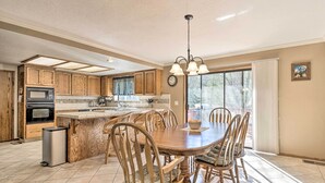 A spacious kitchen with wooden cabinets, a central island, and a dining area with wooden chairs. - Deck & Hot Tub: Rustic Groveland Home! (Groveland)