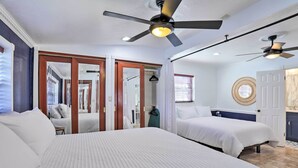 Une chambre d’hôtel avec deux lits, des ventilateurs de plafond, une salle de bain avec un miroir rond et une vue sur l’extérieur.