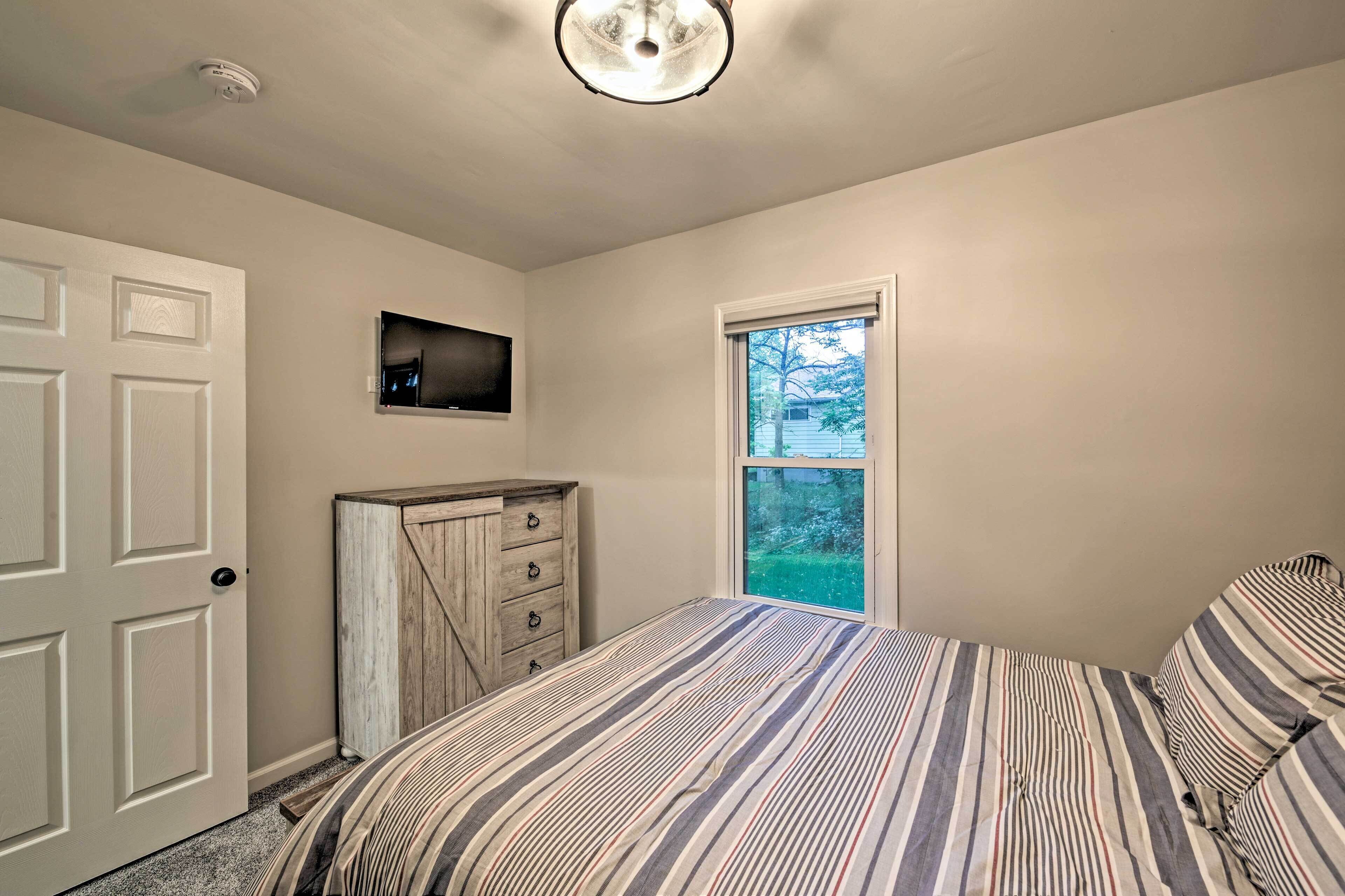A bedroom with a bed, a dresser, a television, and a window.