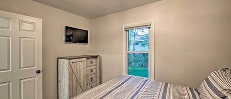 A bedroom with a bed, a dresser, a television, and a window.