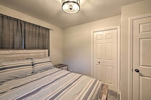 A bedroom with a bed, a nightstand, a window with curtains, and a door. - Updated Twin Lakes Cottage, Walk to Lake Mary (Twin Lakes)