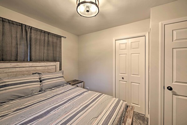 A bedroom with a bed, a nightstand, a window with curtains, and a door. - Updated Twin Lakes Cottage, Walk to Lake Mary (Twin Lakes)