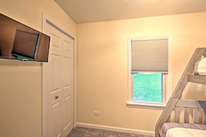 A room with a door, a window with blinds, a TV mounted on the wall, and a wooden staircase.