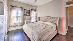 Une chambre avec un grand lit, un ventilateur de plafond, une fenêtre avec des rideaux légers et un radiateur.