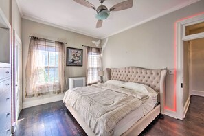 Un dormitorio con una cama grande, un ventilador de techo, una ventana con cortinas traslúcidas y un radiador.