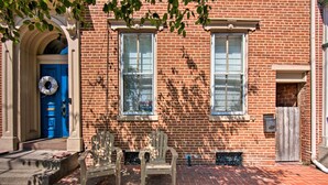 Un bâtiment en briques avec une porte bleue, deux fenêtres et un banc devant.