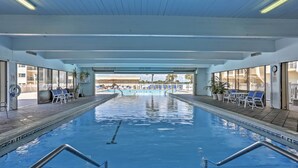Ein Hallenbad mit klarem Wasser, umgeben von Liegestühlen und Topfpflanzen.