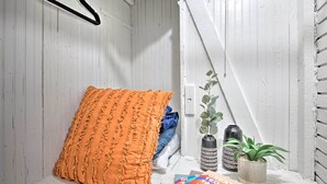 A room with white wooden walls, a hanging black hanger, an orange textured pillow, a blue blanket, a potted plant, and two decorative vases. - Modernized SLC Duplex w/ Yard ~ 4 Mi to Dtwn! (Salt Lake City)