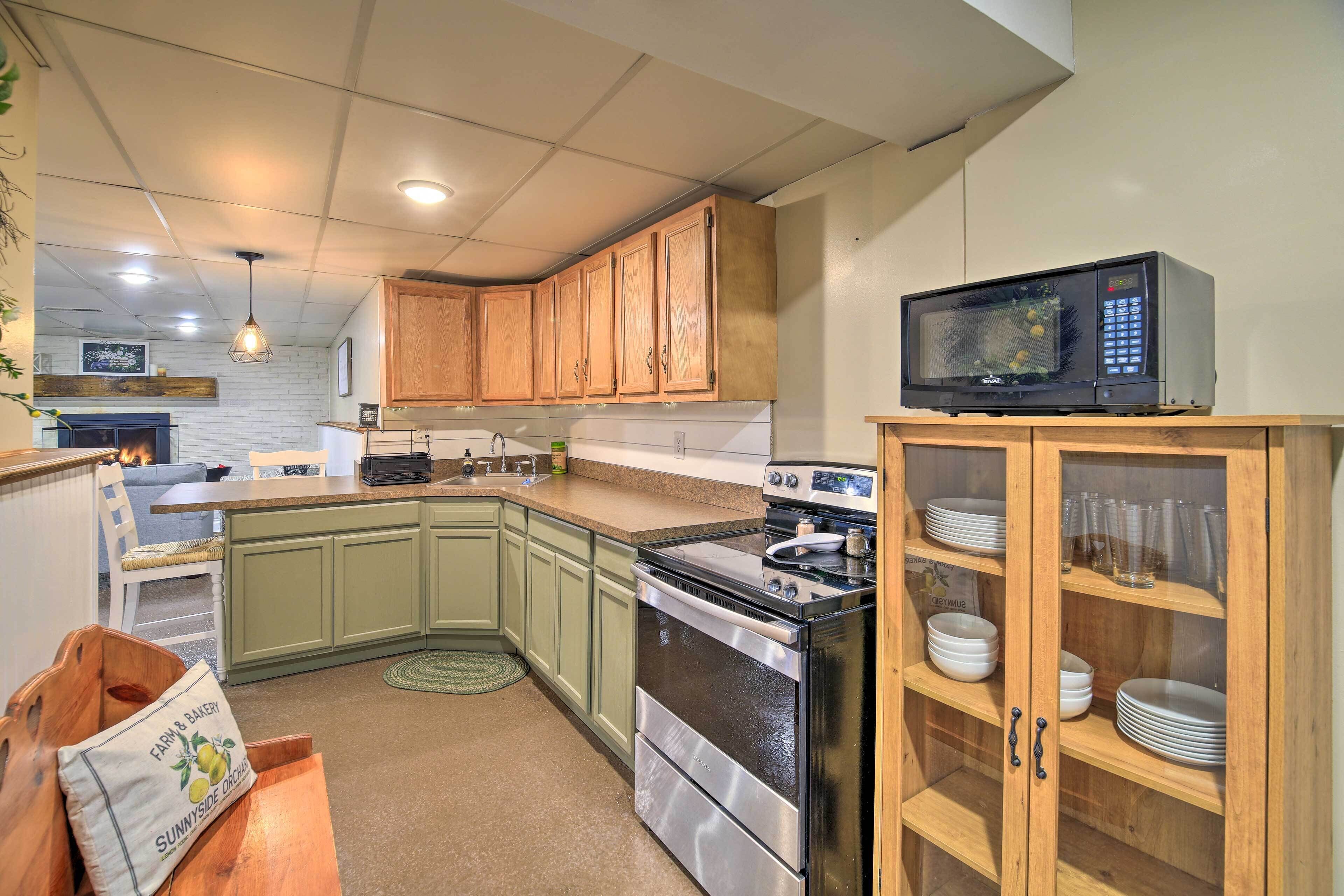 A kitchen with green cabinets, a microwave, a stove, and a cabinet with dishes.