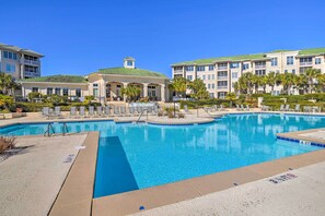 A large outdoor swimming pool surrounded by lounge chairs and a building with balconies.