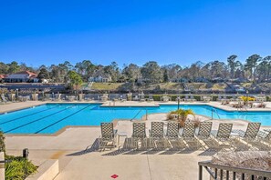 A swimming pool with multiple lanes, surrounded by lounge chairs and a view of houses in the background.