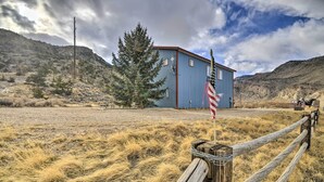 A blue building with a red roof, surrounded by dry grass and a wooden fence. - 'cedar Mountain Hideout' By Cody Night Rodeo! (Cody)