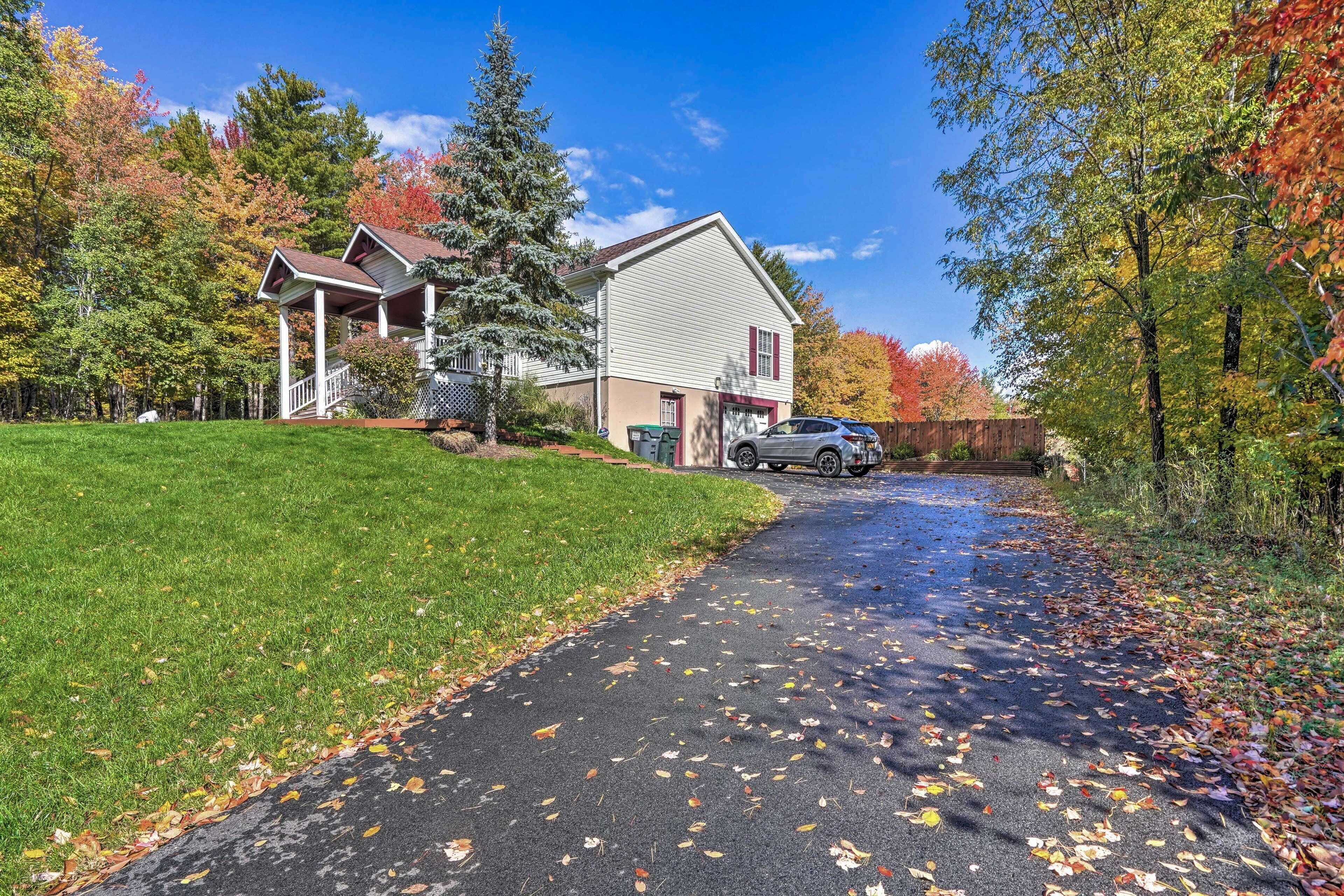 A two-story house with a covered porch, a driveway with fallen leaves, and a car parked in front.