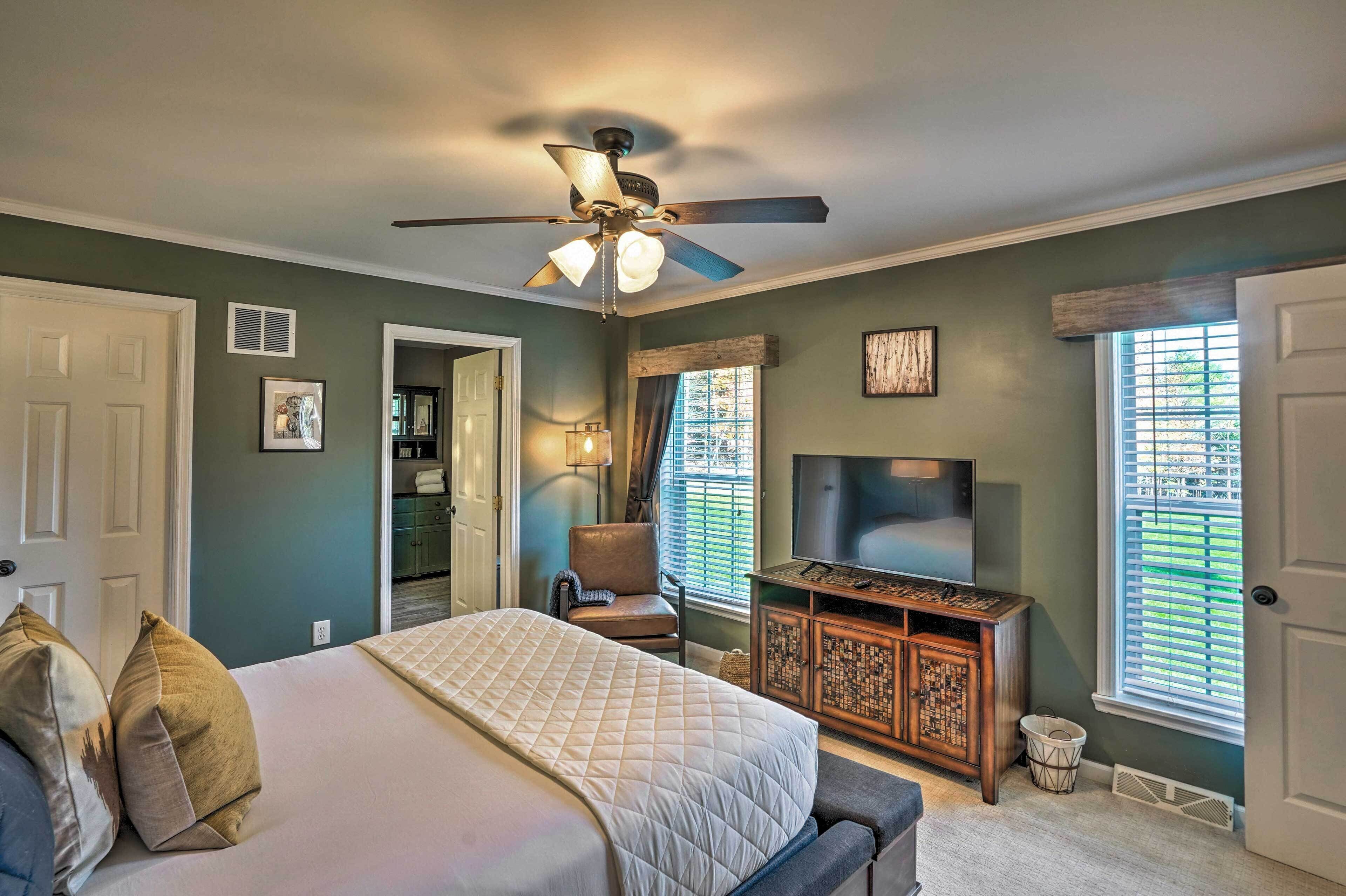 A bedroom with a bed, a ceiling fan, a TV, and a window with blinds.