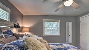Een slaapkamer met een bed, een plafondventilator, een raam met jaloezieën en een deur.
