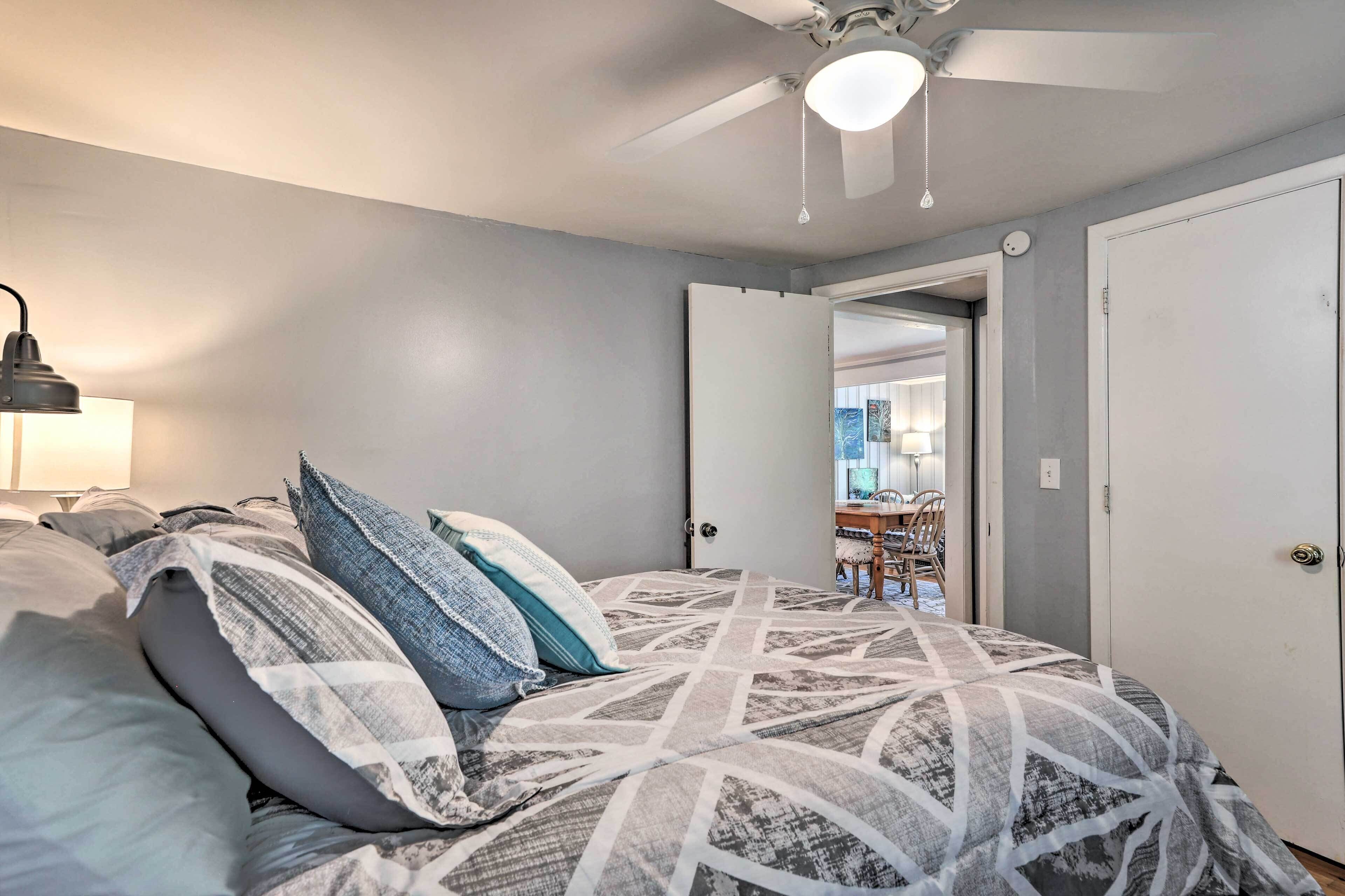 A bedroom with a bed, a ceiling fan, a door, and a view into another room.