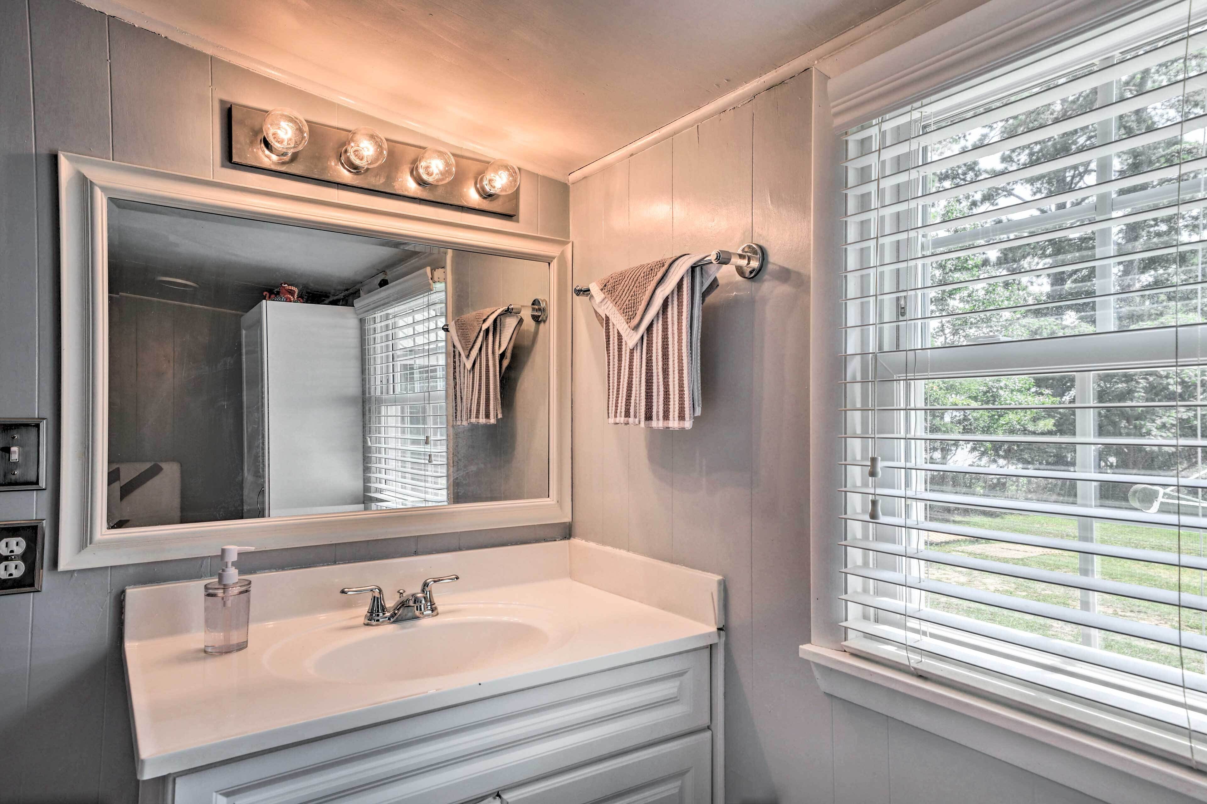 A bathroom with a large mirror, a white sink, and a window with blinds.