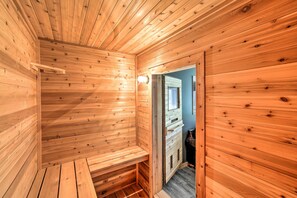 Een houten sauna met banken en een deur naar een andere ruimte.