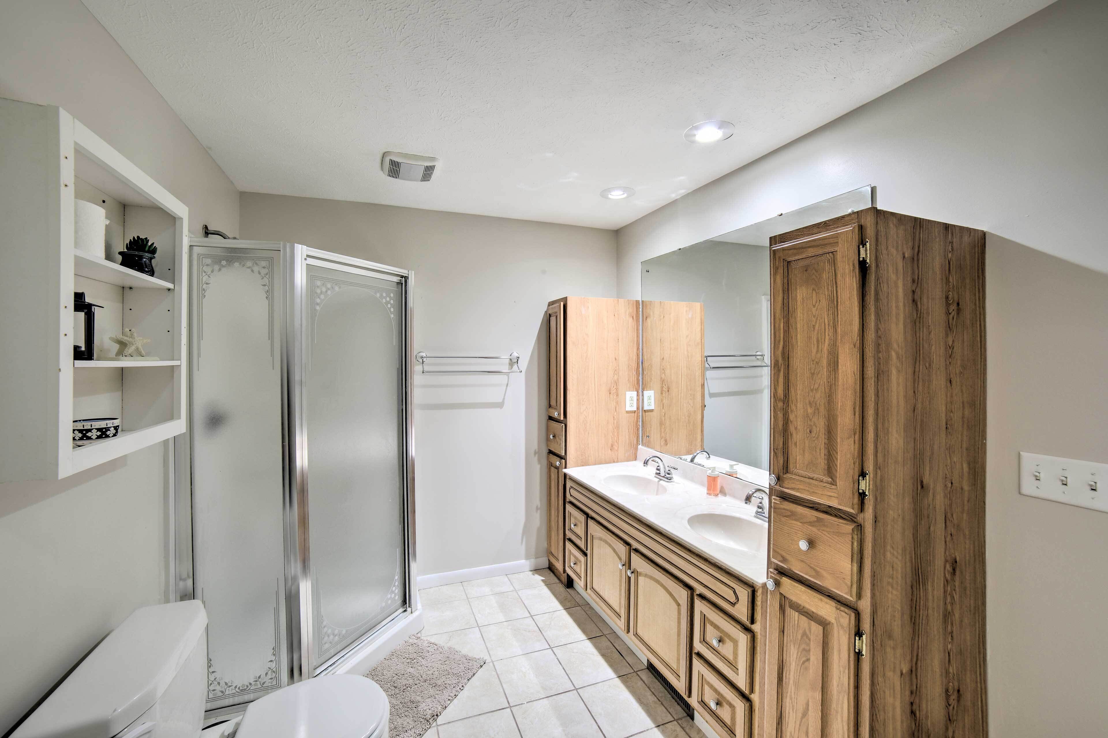 A modern bathroom with a glass shower enclosure, a white toilet, wooden cabinets, and a large mirror.