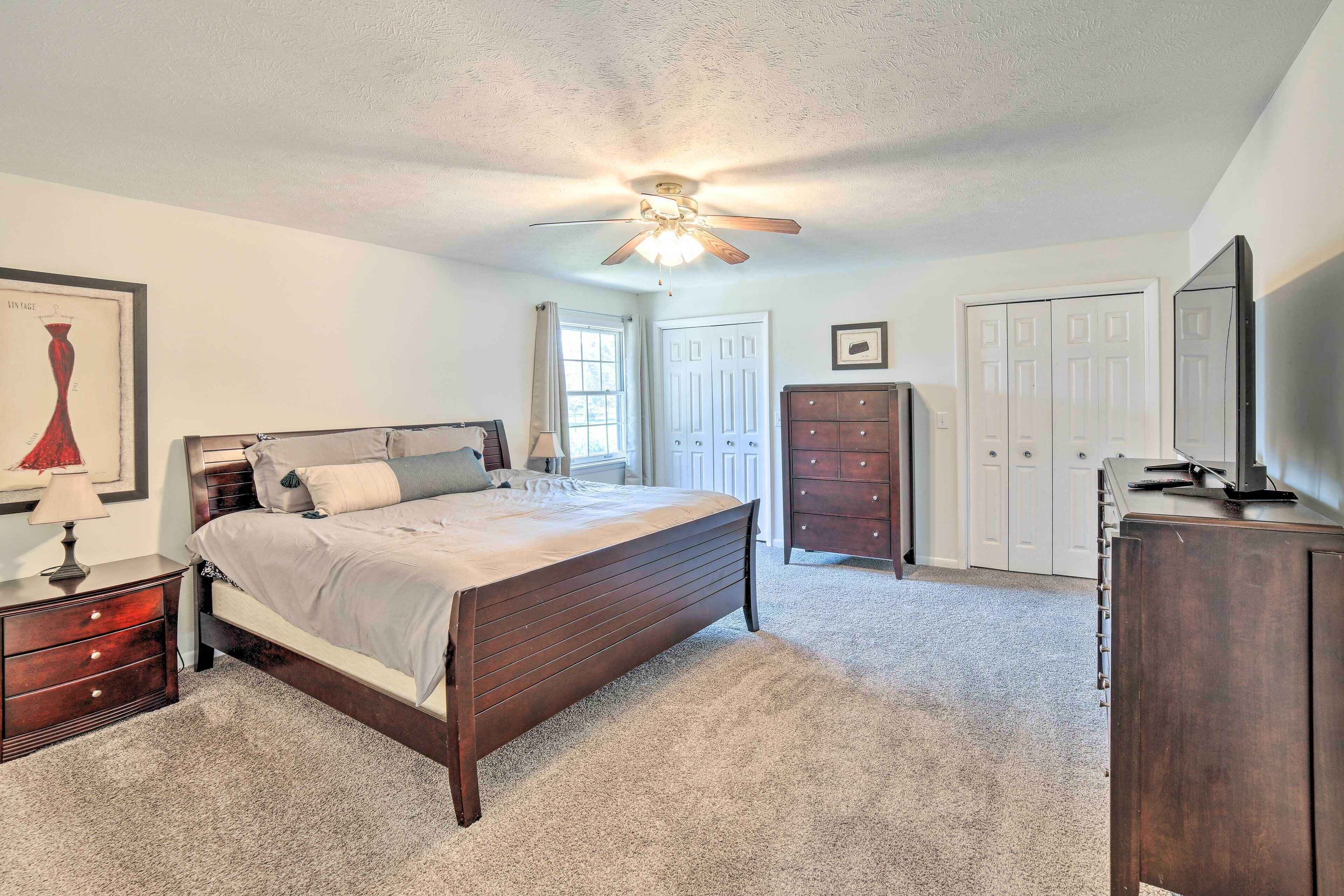 Quarto com cama de madeira, cômoda, espelho e ventilador de teto.