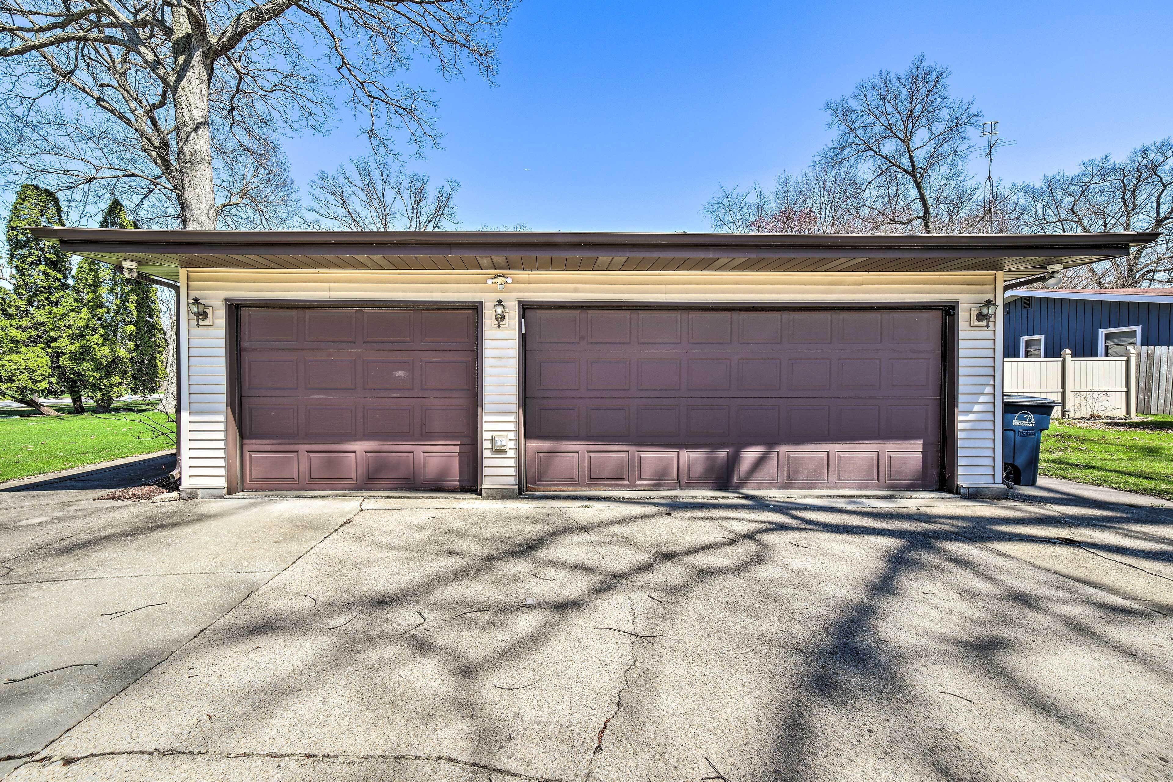 A garage with two large doors, a covered driveway, and a house in the background.
