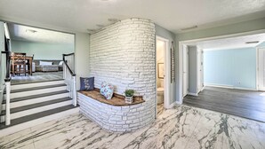 Un vaste espace de vie agrémenté d’un mur en briques blanches aux lignes courbes, d’un banc en bois avec des coussins et d’un sol en marbre.